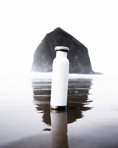 white bq bottle on beach with large rock